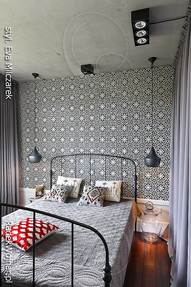 Fotografia szarej sypialni z metalowym łóżkiem, betonowym sufitem, zasłonami i czarnymi wiszącymi lampami.