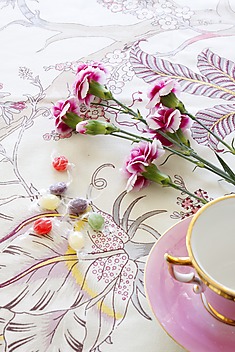 wycinek przykrytego obrusem stołu z filiżanką, kwiatami i cukierkami 