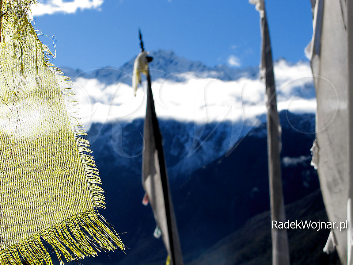 Ośnieżone Himalaje widoczne przez tybetańskie flagi i maszty modlitewne