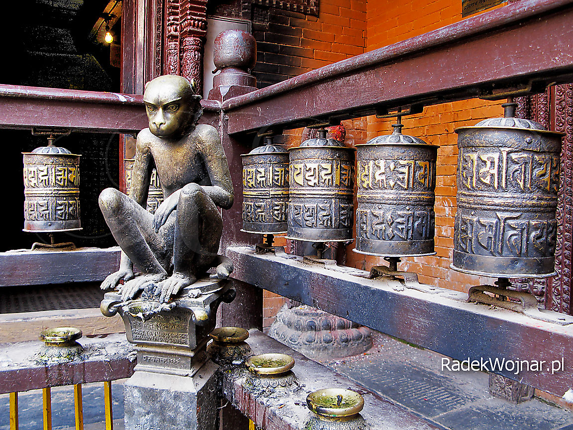 Zamyślona małpa-rzeźba na dziedzińcu świątyni pośród modlitewnych młynków
