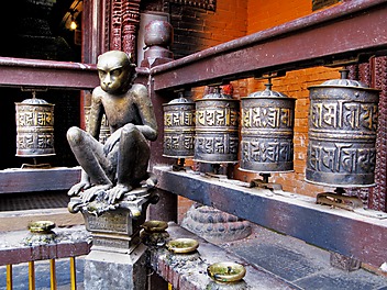 Zamyślona małpa-rzeźba na dziedzińcu świątyni pośród modlitewnych młynków